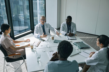 High angle view at group of doctors sitting at meeting table in conference room during medical...