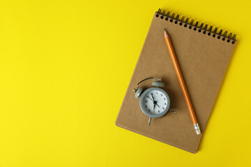 Alarm clock, notebook and pencil on yellow background