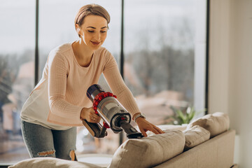 Young woman with rechargeable vacuum cleaner cleaning at home © Petro