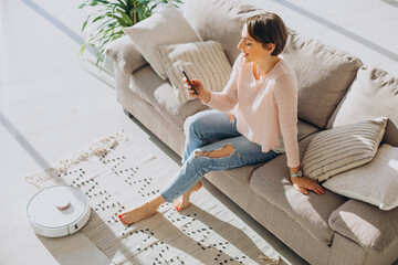 Woman relaxing on sofa while robot vacuum cleaner doing housework