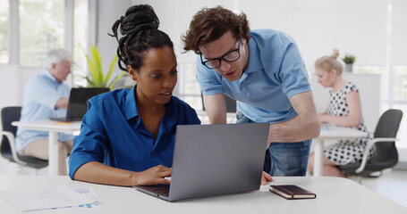 Fototapeta premium Diverse male and female business colleague in discussion at desk in office looking at laptop