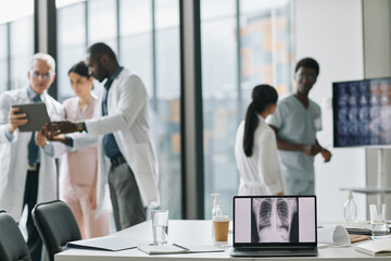 Diverse group of doctors collaborating in conference room with focus on laptop screen in foreground, copy space
