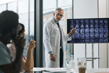 Waist up portrait of mature doctor giving presentation at medical conference and pointing at x-ray images, copy space