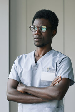 Vertical portrait of confident African-American doctor wearing uniform while standing with arms crossed in clinic