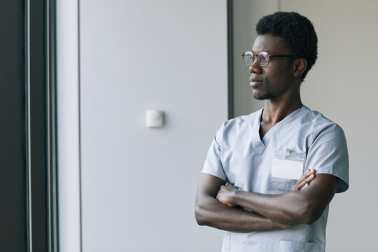 Waist up portrait of confident African-American doctor wearing uniform while standing with arms crossed in clinic, copy space