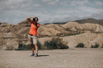 Sports woman photographer taking photos in Tabernas Desert, Spain, in a sunny day, with an orange color t-shirt.