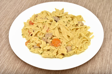 Close-up of Italian traditional tagliatelle pasta with creamy sauce, pork pieces carrot slices and chopped parsley on the white plate. Selective focus.