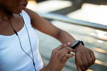 Young african woman training outdoors. Female runner using smart watch.