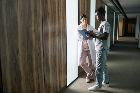 Full length portrait of young African-American medic talking to female colleague in clinic