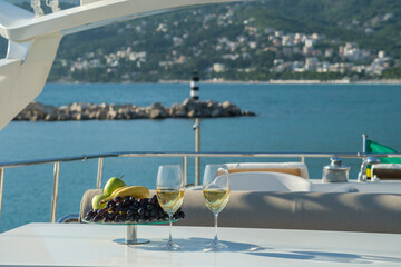 Yacht cruise. A table is set on the deck, there are glasses of white wine and a dish of fruit on...
