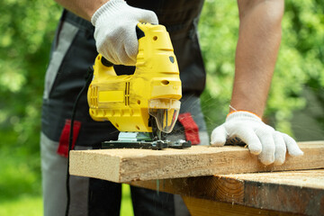 Close-up male carpenter cuts a wooden board using an electric jigsaw