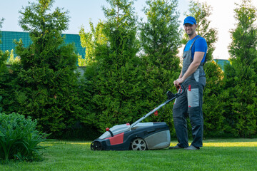 Young gardener in overalls uses a lawn mower on the plot