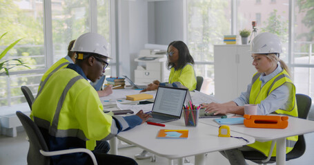 Diverse group of engineers in safety uniform and hardhat working in modern office
