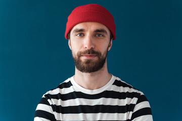 Close up view. On a blue background, a man in a red hat and turtleneck