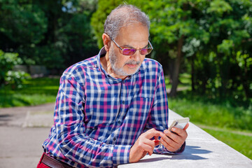 Serious Pensioner with Casual Clothing Glasses and Phone in Park