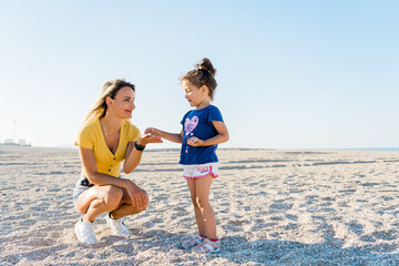 Portrait of a young mother and her daughter on the beach - giving concept, education, spending time together