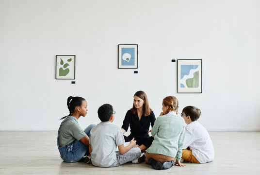 Full length view at diverse group of children sitting in circle during class in art gallery, copy space