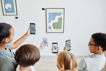 High angle view at diverse group of children holding smartphones in art gallery and taking photos...