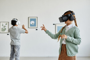 Minimal side view at cute girl wearing VR headset in art gallery while enjoying immersive...