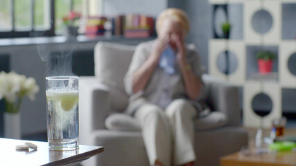 Sick elderly woman coughing and holding head on background of medicine drug in glass
