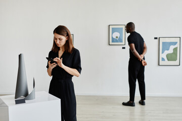 Minimal portrait of elegant young people looking at abstract paintings and sculptures in modern art gallery, copy space