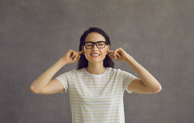 I can't hear you. Head shot of young woman in glasses closing eyes and plugging ears with fingers...