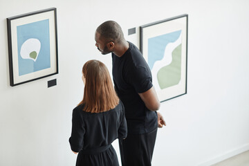 High angle portrait of elegant couple looking at paintings in modern art gallery, copy space