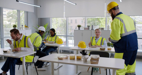 Group of diverse engineers and workers enjoy eating food and relax in canteen