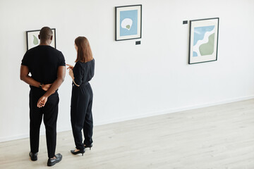 Minimal full length view at elegant couple looking at abstract paintings in modern art gallery, copy space