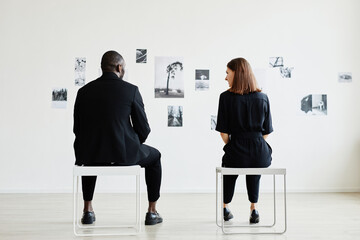 Full length back view at elegant couple looking at black and white photographs in modern art...