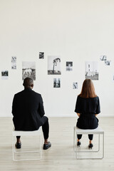 Graphic back view at elegant couple looking at black and white photographs in modern art gallery,...