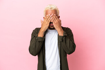Young Colombian handsome man isolated on pink background covering eyes by hands
