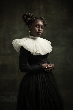 Portrait of medieval African young woman in black vintage dress with big white collar posing isolated on dark green background.