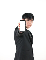 Asian man in a black suit standing and showing a blank screen smartphone on white background. Selective focus on phone.