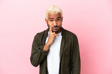 Young Colombian handsome man isolated on pink background and thinking
