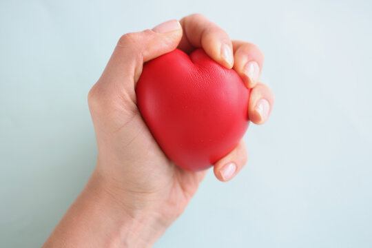 Female hand holding red toy heart on blue background closeup