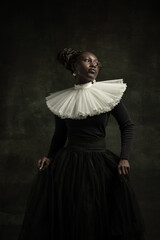 Medieval African young woman in black vintage dress with big white collar posing isolated on dark...