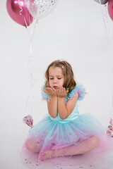 beautiful little girl in a festive dress is sitting and blowing confetti on a white background with...