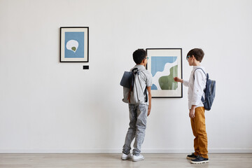 Minimal back view portrait of two schoolboys looking at abstract paintings in modern art gallery,...