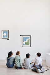 Vertical wide angle view at diverse group of children sitting on floor in modern art gallery and...