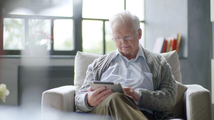 Senior man using digital tablet sitting on the couch at home