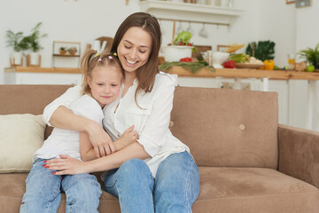 Obraz premium The little girl complains to her mother and cries. A young woman calms her daughter on the couch at home