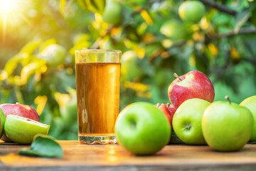Fresh apple juice and apples on wooden table in the summer orchard garden.