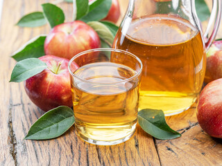 Glass and carafe of fresh apple juice and organic apples on dark old wooden table.