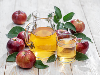 Glass of juice and carafe of fresh apple juice and organic apples on wooden table.