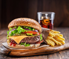 Delicious burger with cola and potato fries on a wooden table with a dark brown background behind. Fast food concept.