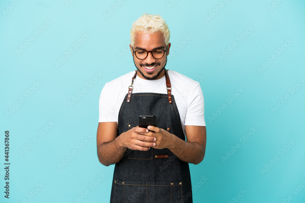 Wall mural Restaurant Colombian waiter man isolated on blue background sending a message with the mobile