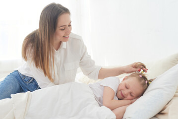 Obraz na płótnie Canvas Beautiful young mom wakes up her preteen little daughter in the morning. Tenderness and care. Mother's love