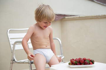White child eats strawberries in summer sitting on the terrace