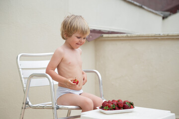 Happy child eats strawberries in summer sitting on the terrace